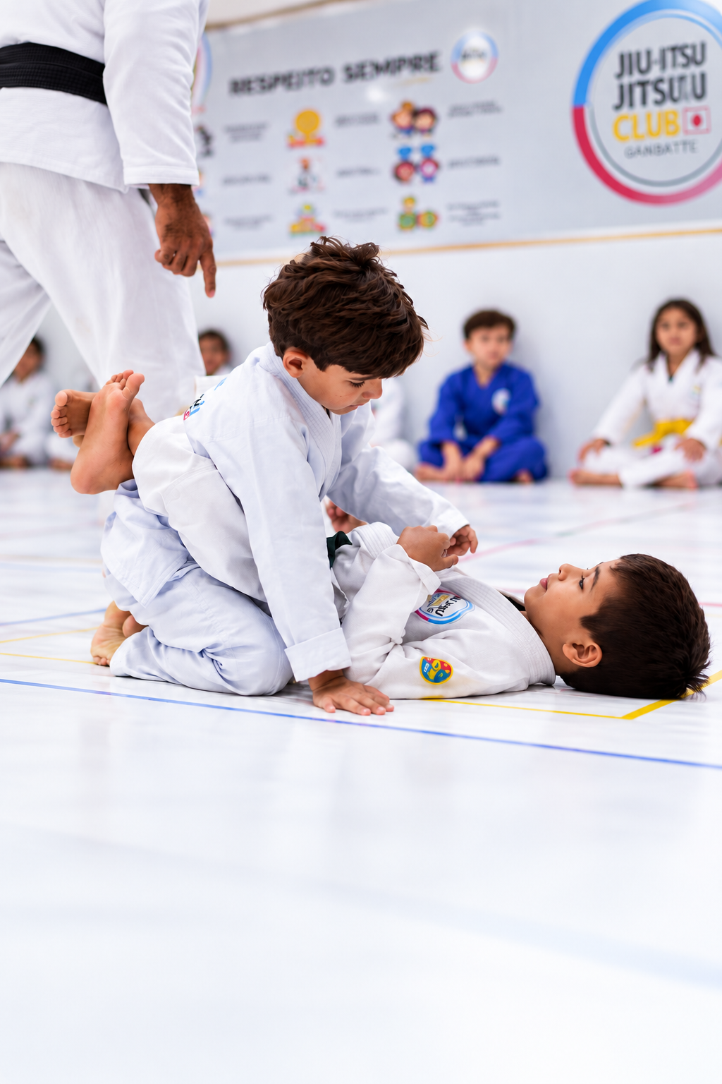 Dois alunos da Jiu Jitsu Club praticando no tatame, com o professor e colegas ao fundo